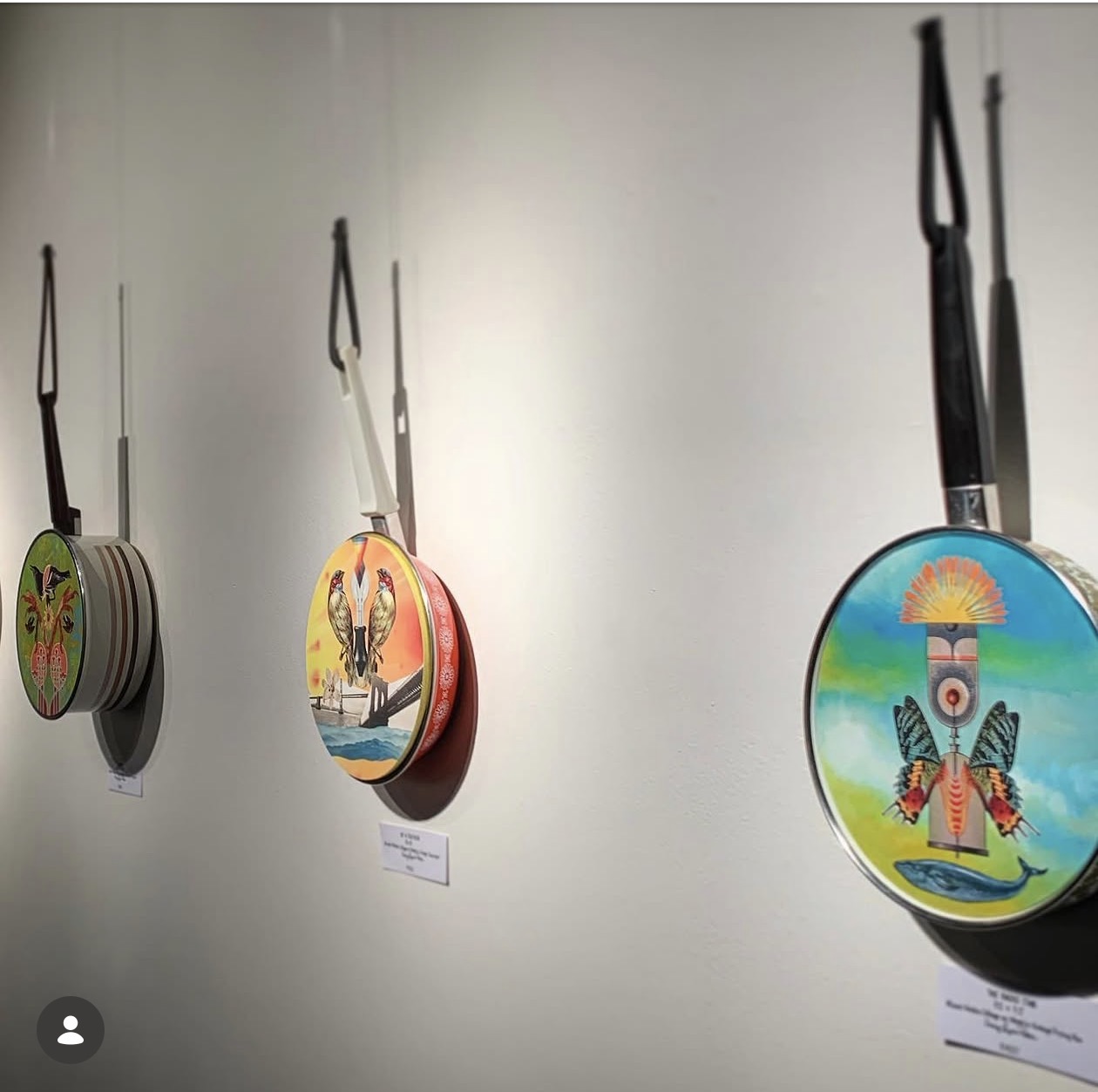 Colorful mixed-media artworks on hanging pans displayed on a gallery wall
