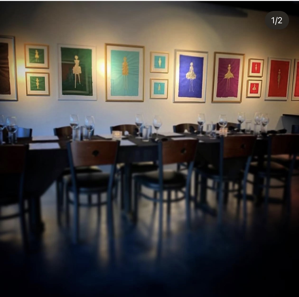 Colorful framed figure artworks above tables set with wine glasses at The Gallery