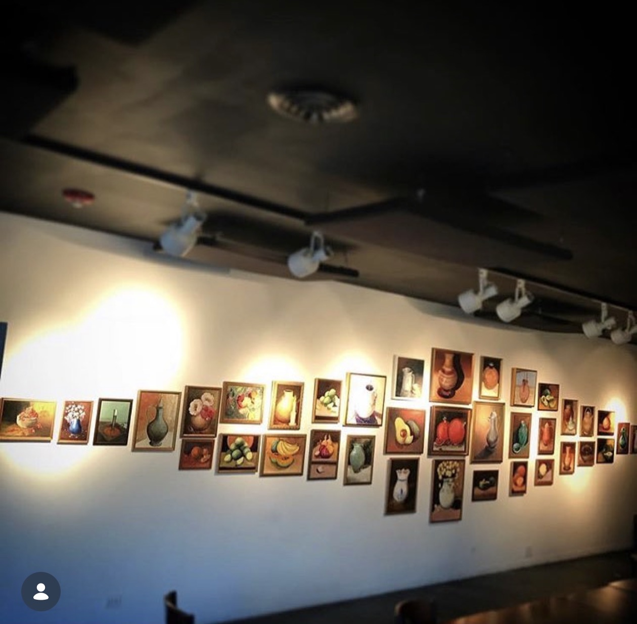 A long salon-style display of small framed still-life paintings at The Gallery